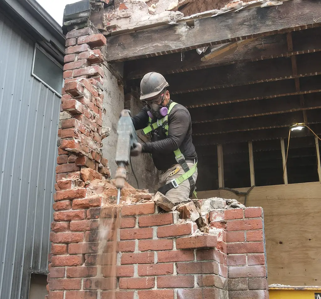 MAGCOR worker taking down a brick wall by hand during a manual demolition