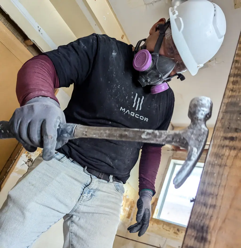 MAGCOR worker removing a wood beam by hand with a pry bar